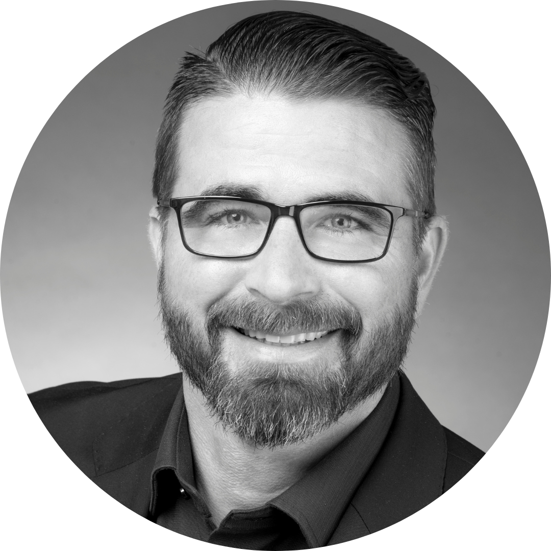 A man with a beard and glasses is smiling in a black and white photo.