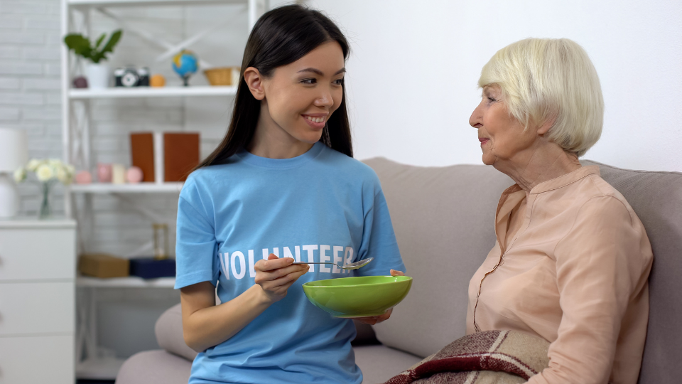 Young volunteer feeding old woman nursing home, taking care of hospice patient
