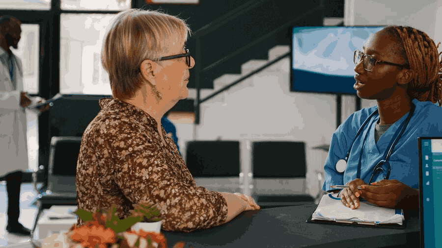 A nurse is talking to an older woman in a hospital waiting room.