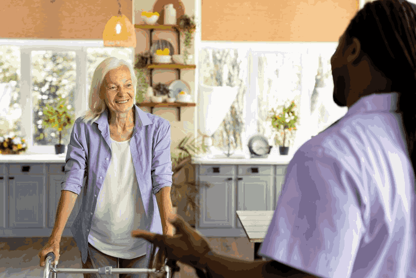 A man is helping an elderly woman with a walker in a kitchen.