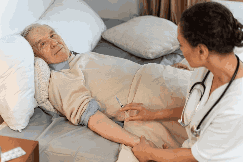 A nurse is talking to an elderly man laying in a bed.