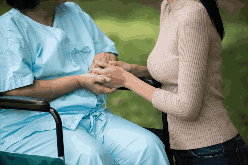 A woman is holding the hand of an elderly woman in a wheelchair.