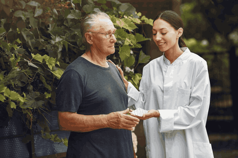 A nurse is giving an elderly man a pill.