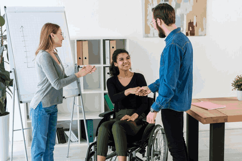 A woman in a wheelchair is shaking hands with a man and a woman.