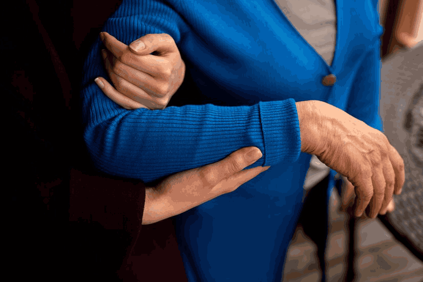 A woman is holding the arm of an older woman in a blue sweater.