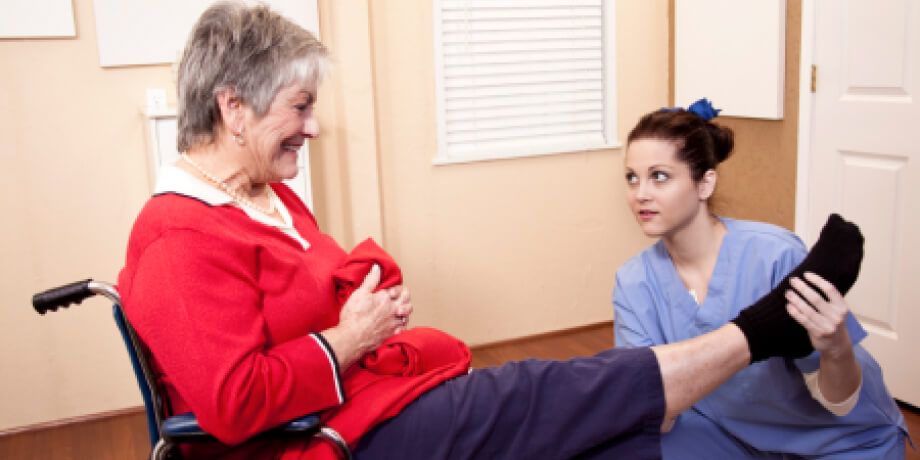 An elderly woman in a wheelchair is being helped by a nurse.