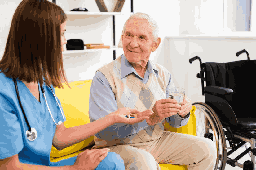 A nurse is giving an elderly man a glass of water and pills.