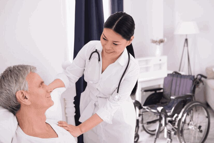 A nurse is talking to an elderly man in a wheelchair in a hospital room.