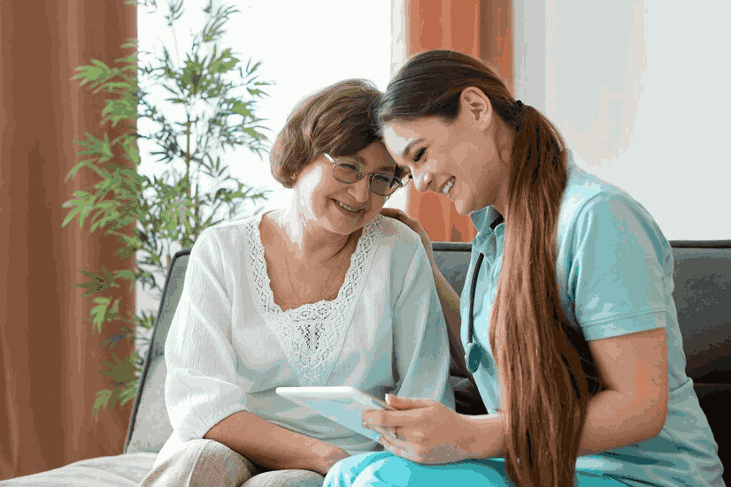 Two women are sitting on a couch looking at a tablet.