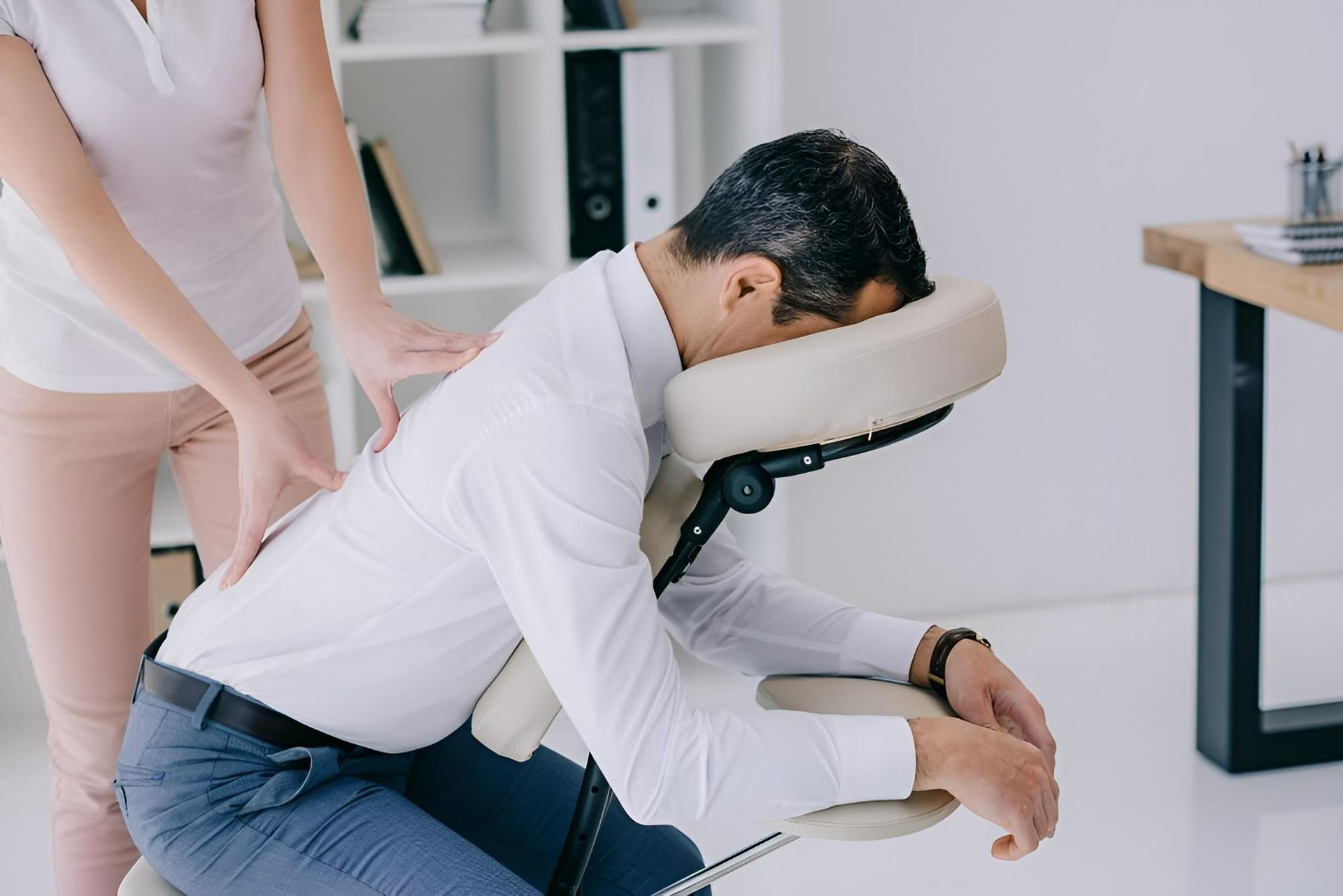 A Man Is Sitting in A Chair Getting a Massage from A Woman — Action Physiotherapy in Cooks Hill, NSW