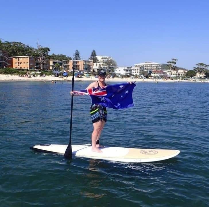 A Person on A Paddle Board Holding an Australian Flag — Action Physiotherapy in Cooks Hill, NSW