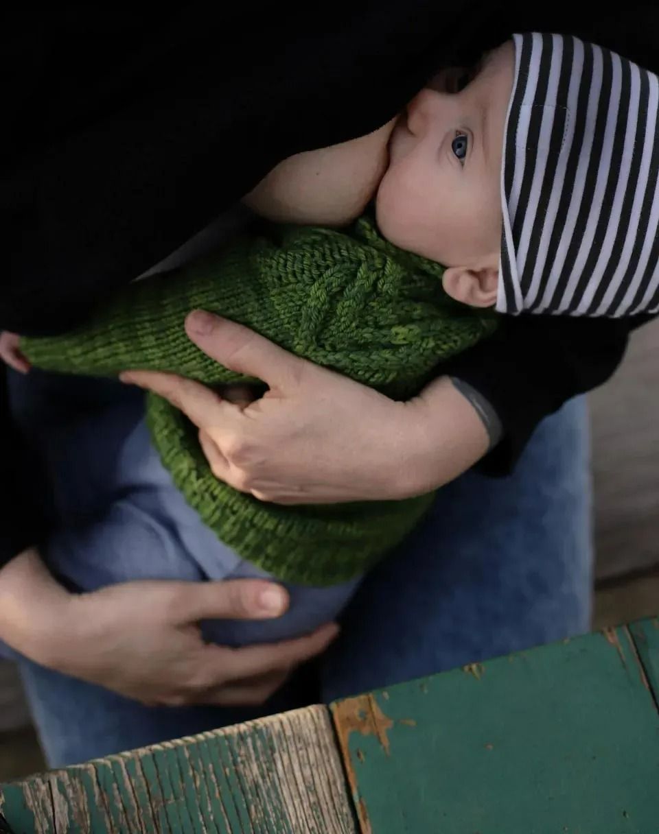 A Woman Is Holding a Baby Wearing a Green Sweater and Striped Hat — Action Physiotherapy in Cooks Hill, NSW