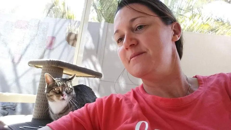A Woman in A Red Shirt Is Sitting Next to A Cat — Action Physiotherapy in Cooks Hill, NSW