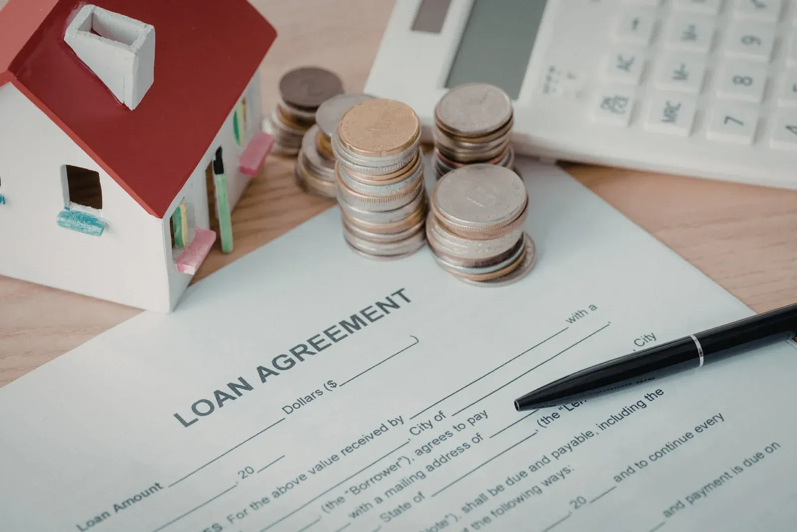 A toy house, stacks of coins, and a pen rest on a blank