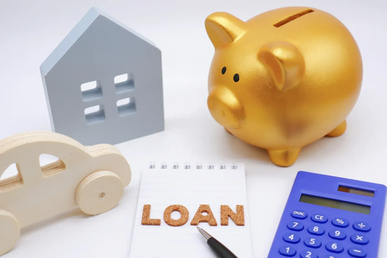 A gold piggy bank, a small house model, a wooden car, a blue calculator, and a notepad with the word