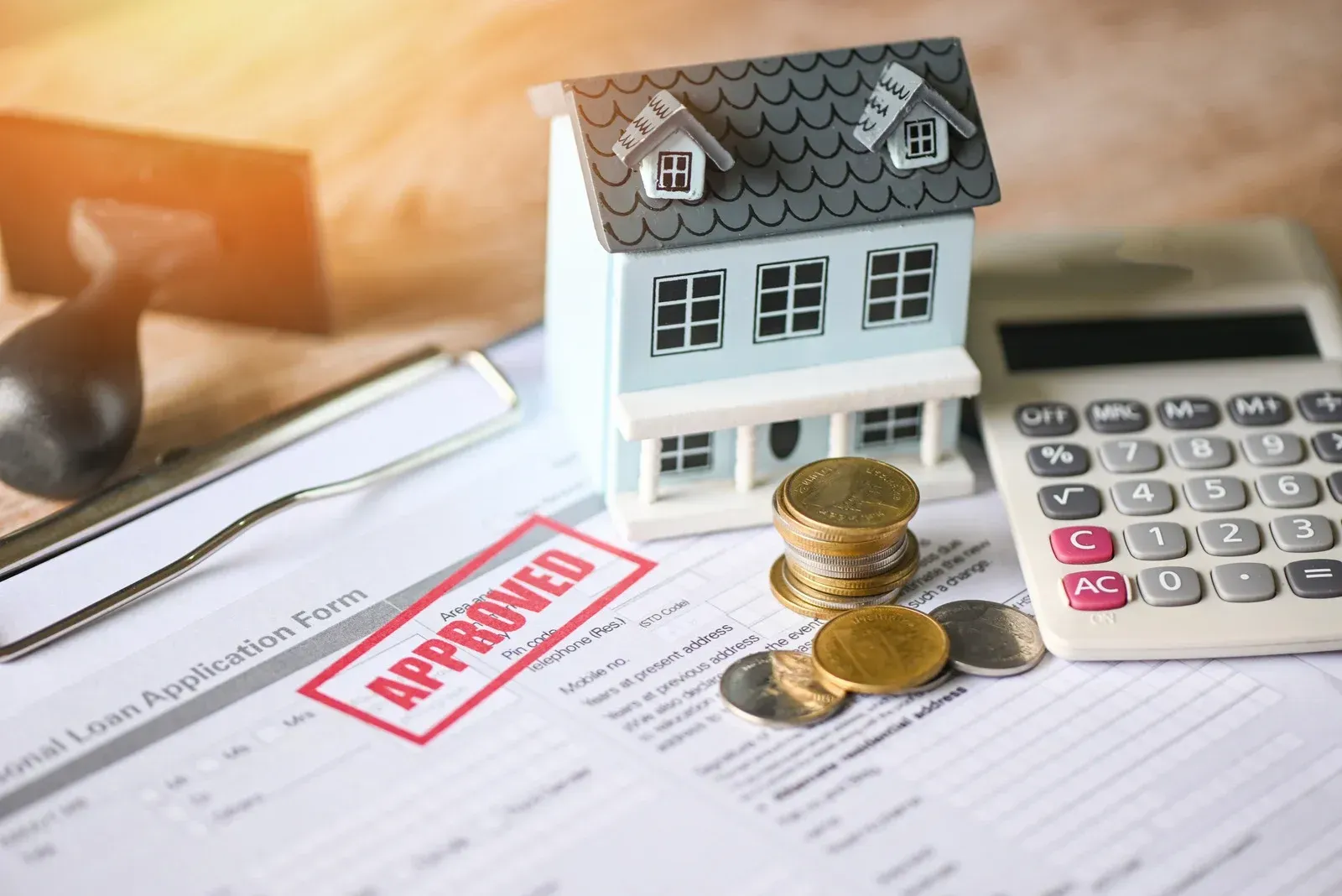 An approved home loan application form with a small house model, coins, and a calculator on a desk.