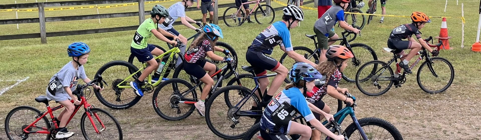 Youth yclists in colorful gear riding closely together on a gravel trail during a race