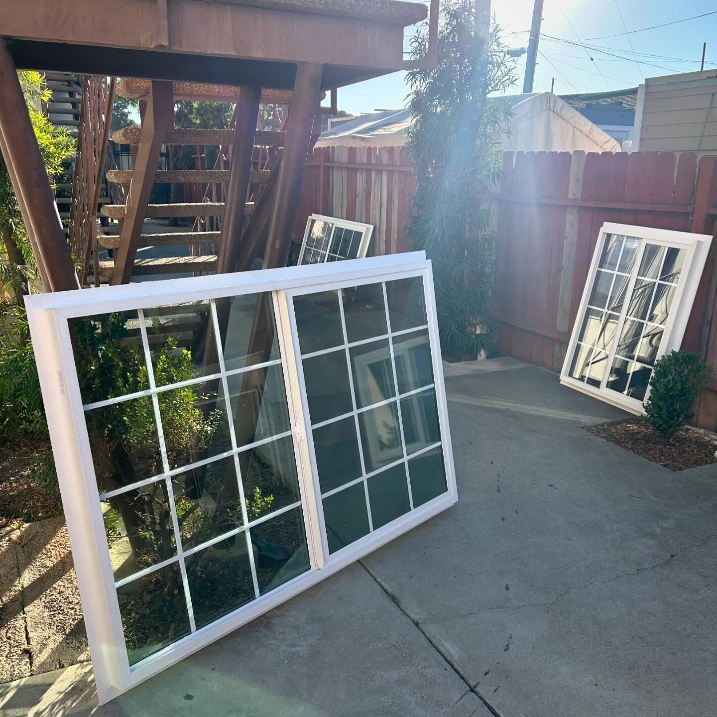 Two white window frames leaning on a driveway beside a wooden fence and deck stairs