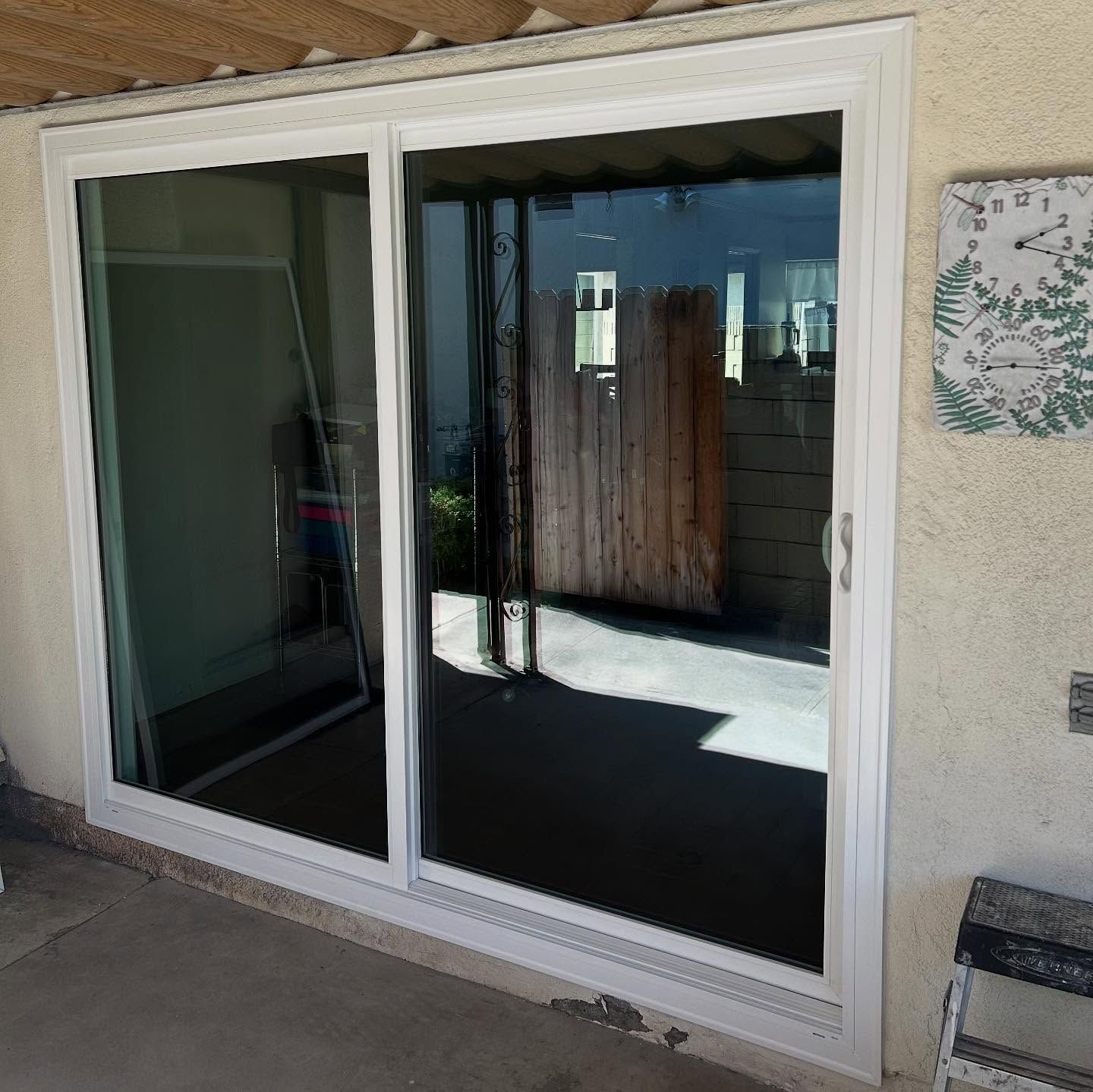 Sliding glass patio door reflecting a sunny backyard and fence