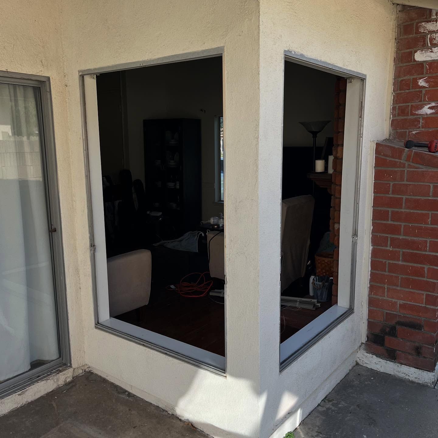 Corner of a beige stucco patio with two open windows and a brick wall