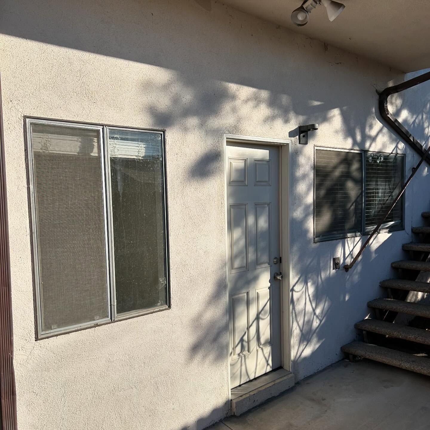 Exterior of a stucco house with windows, a white door, and stairs on the right