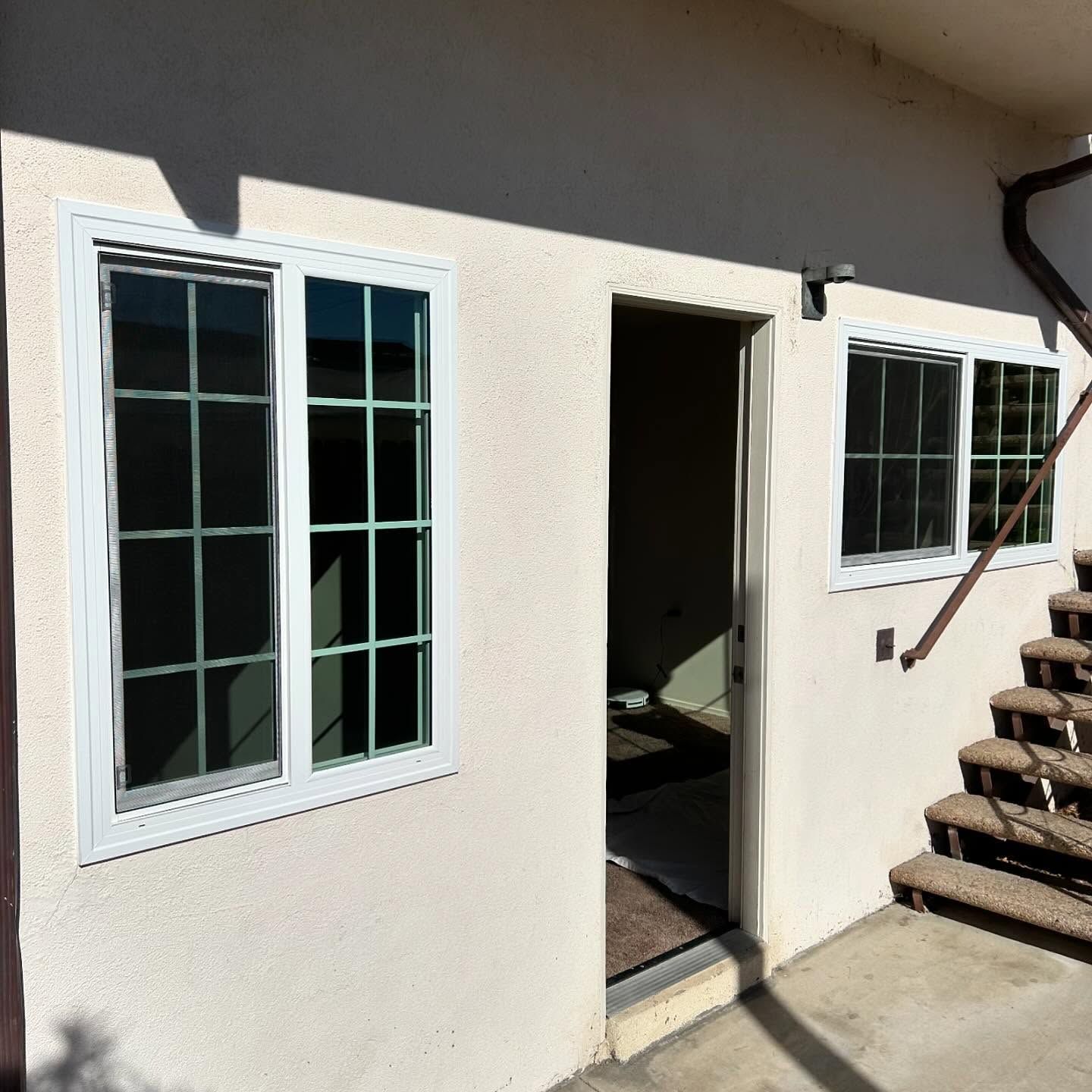 Exterior of a cream house with two windows, an open doorway, and stairs on the right