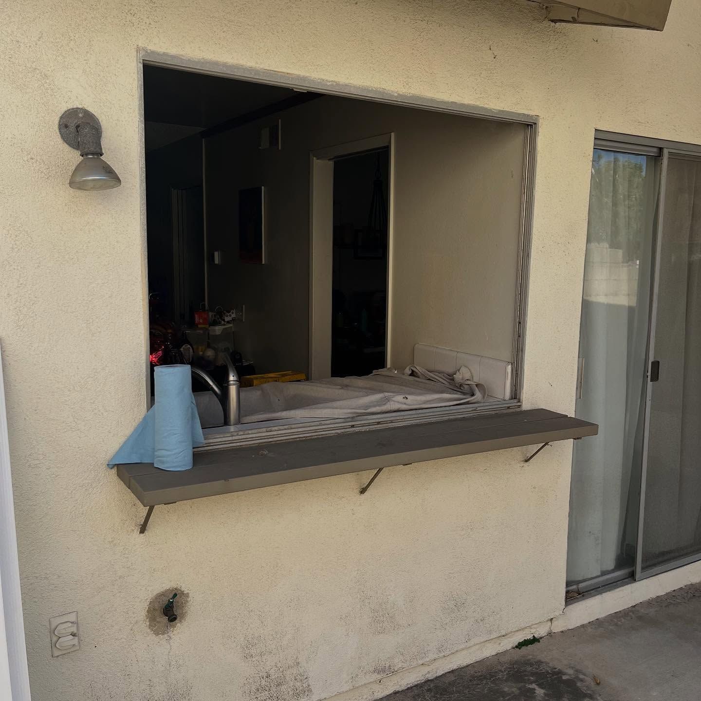 Open apartment window with a countertop, blue container, and sliding glass door beside it.