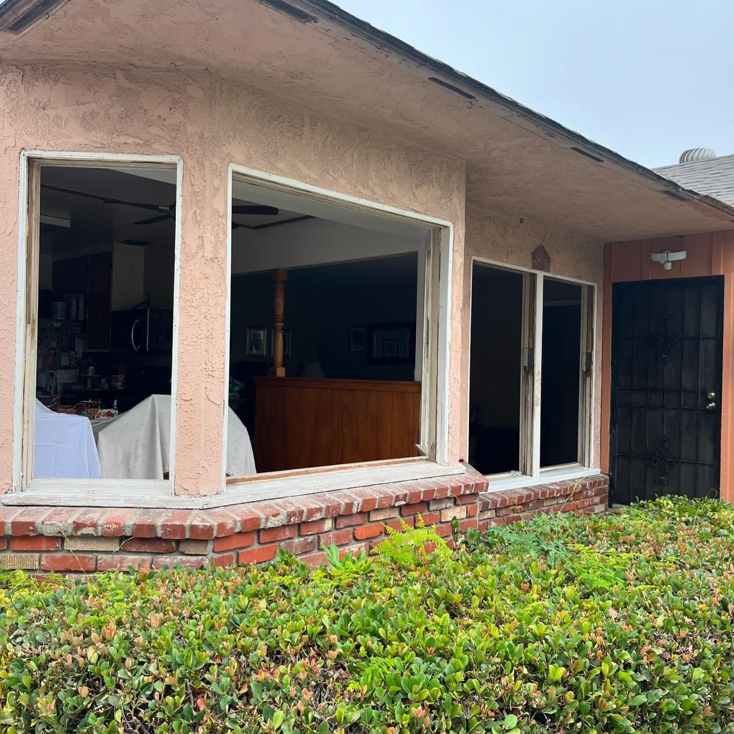 Damaged storefront with broken windows, exposed interior, and overgrown hedge outside.