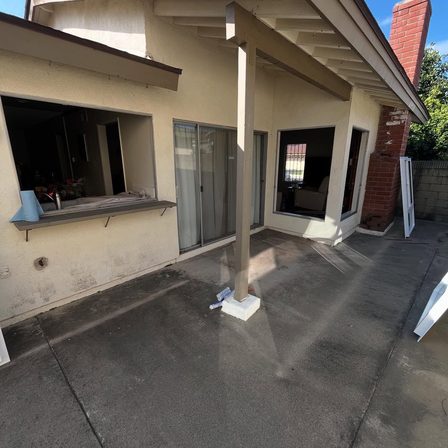 Exterior of a beige house with a covered patio, open windows, and concrete driveway in front