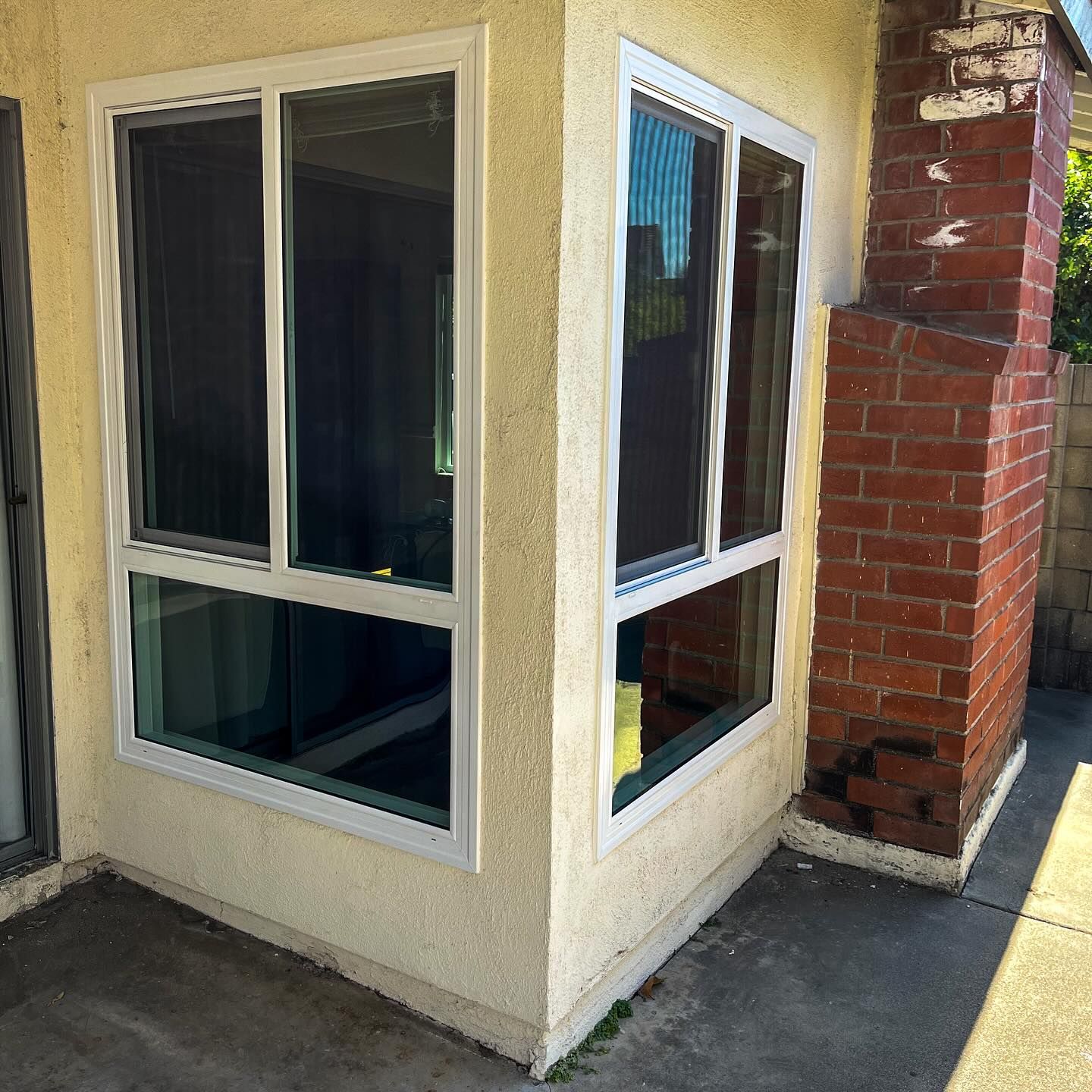 Corner of a stucco house with white-trim windows beside a brick column and concrete walkway