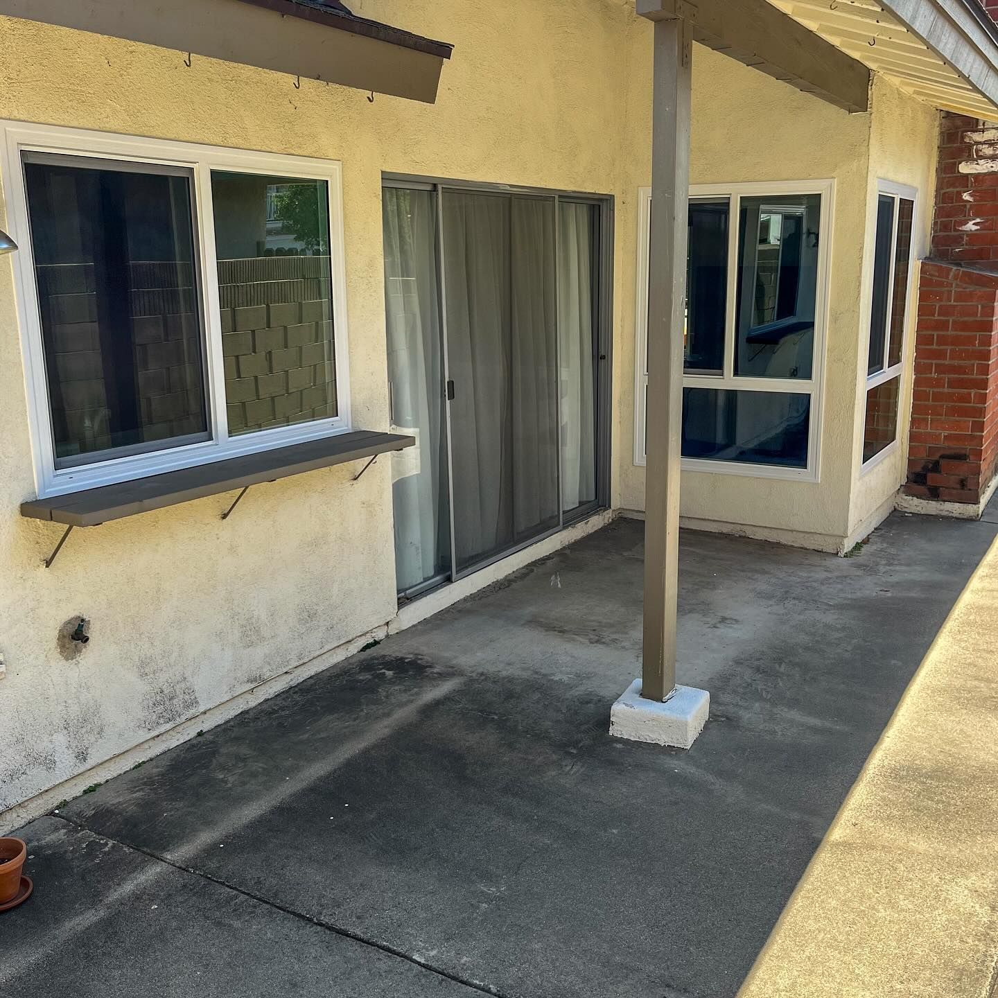 Patio with beige stucco wall, sliding glass door, windows, and a support post on concrete pavement