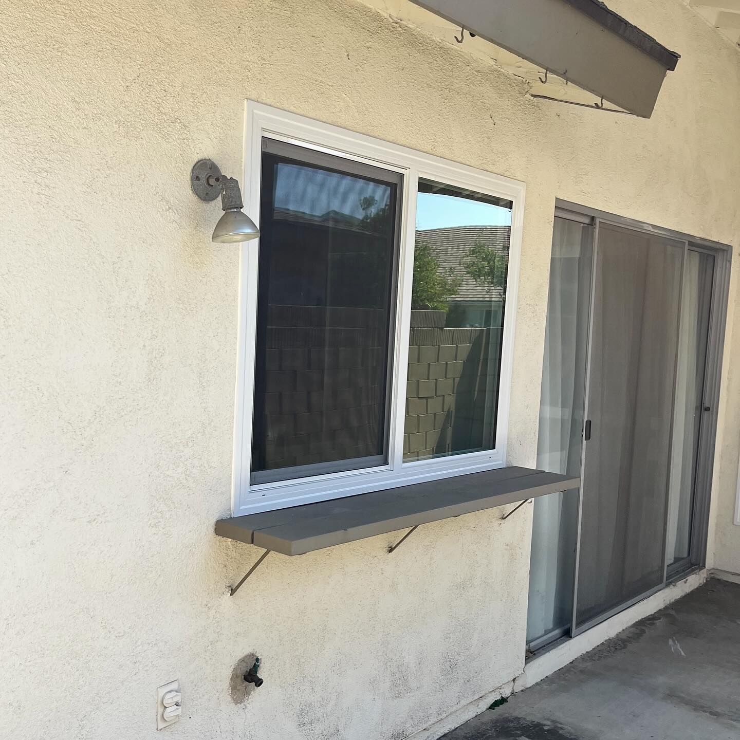 Exterior stucco wall with window, small awning, and sliding glass door by a patio.