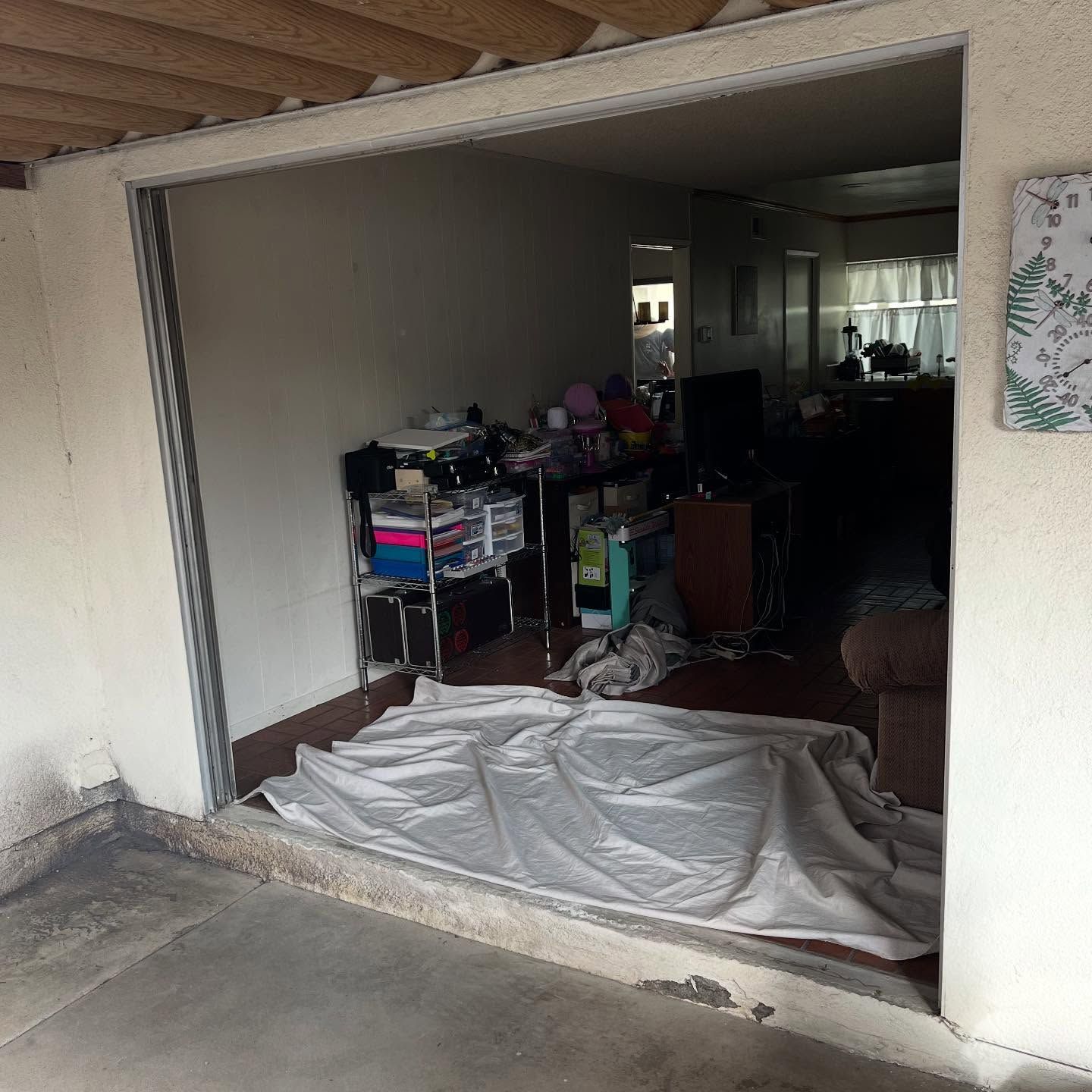 Garage interior with cluttered storage shelves and a white sheet spread on the floor in the doorway