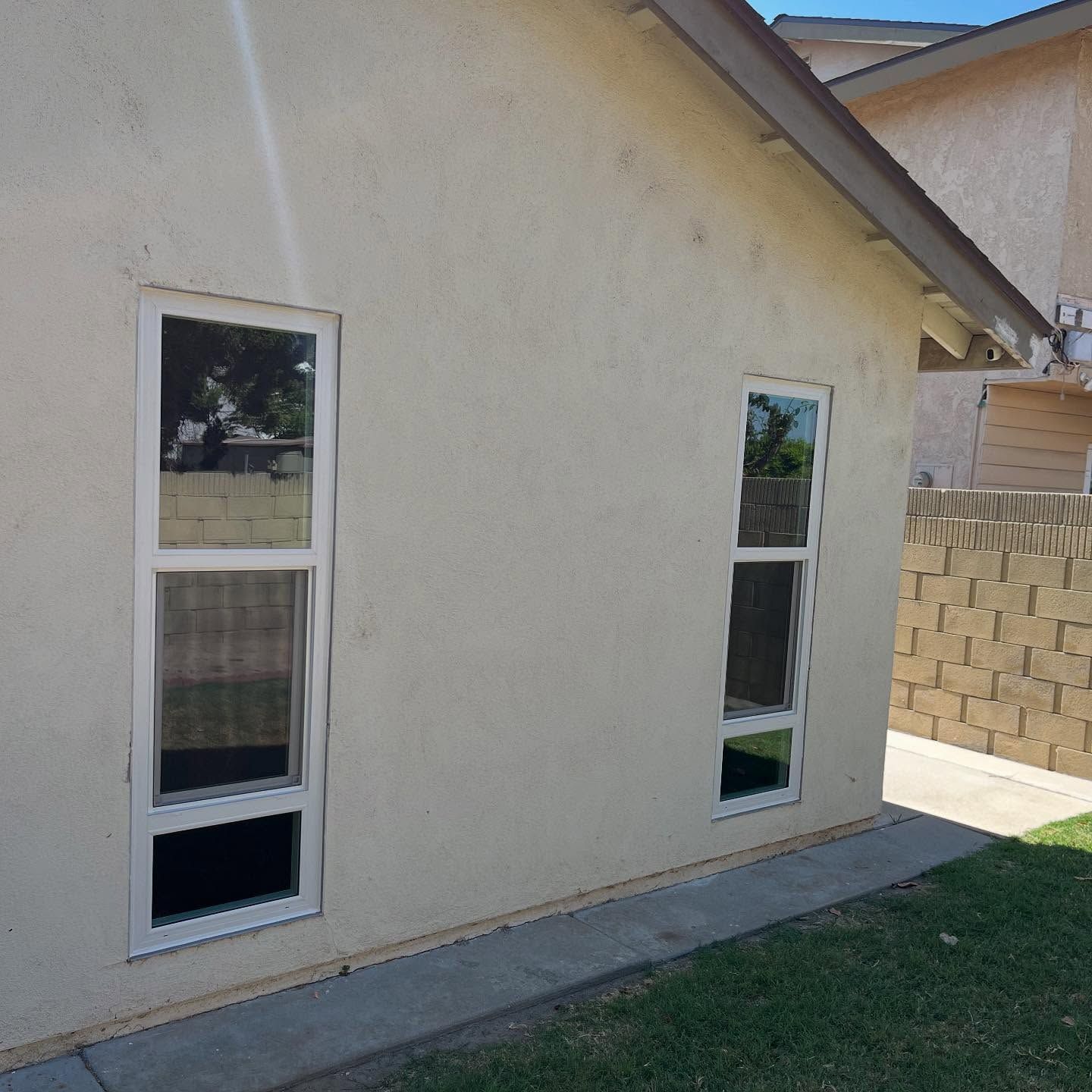 Side of a beige house with two tall narrow windows beside a grass lawn and concrete walkway