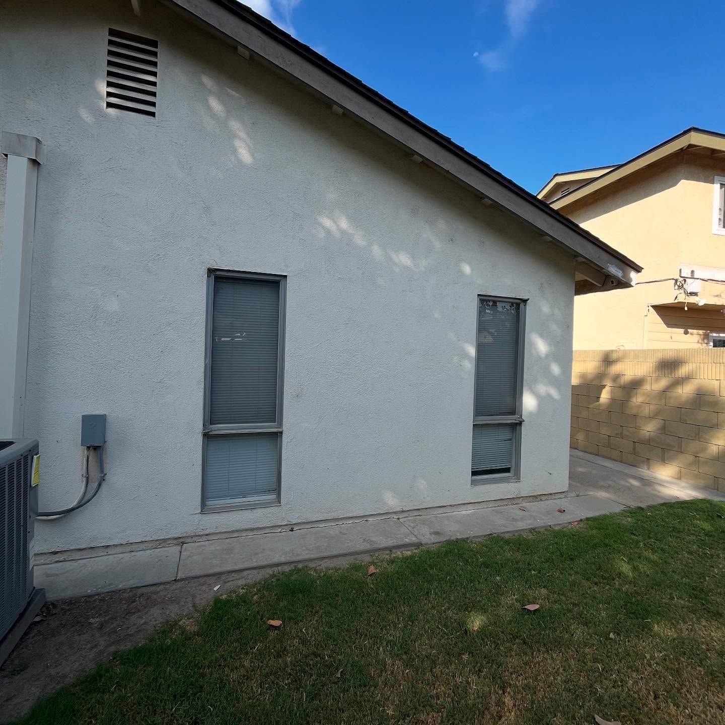 White house exterior with two narrow windows and a small grass yard under a blue sky