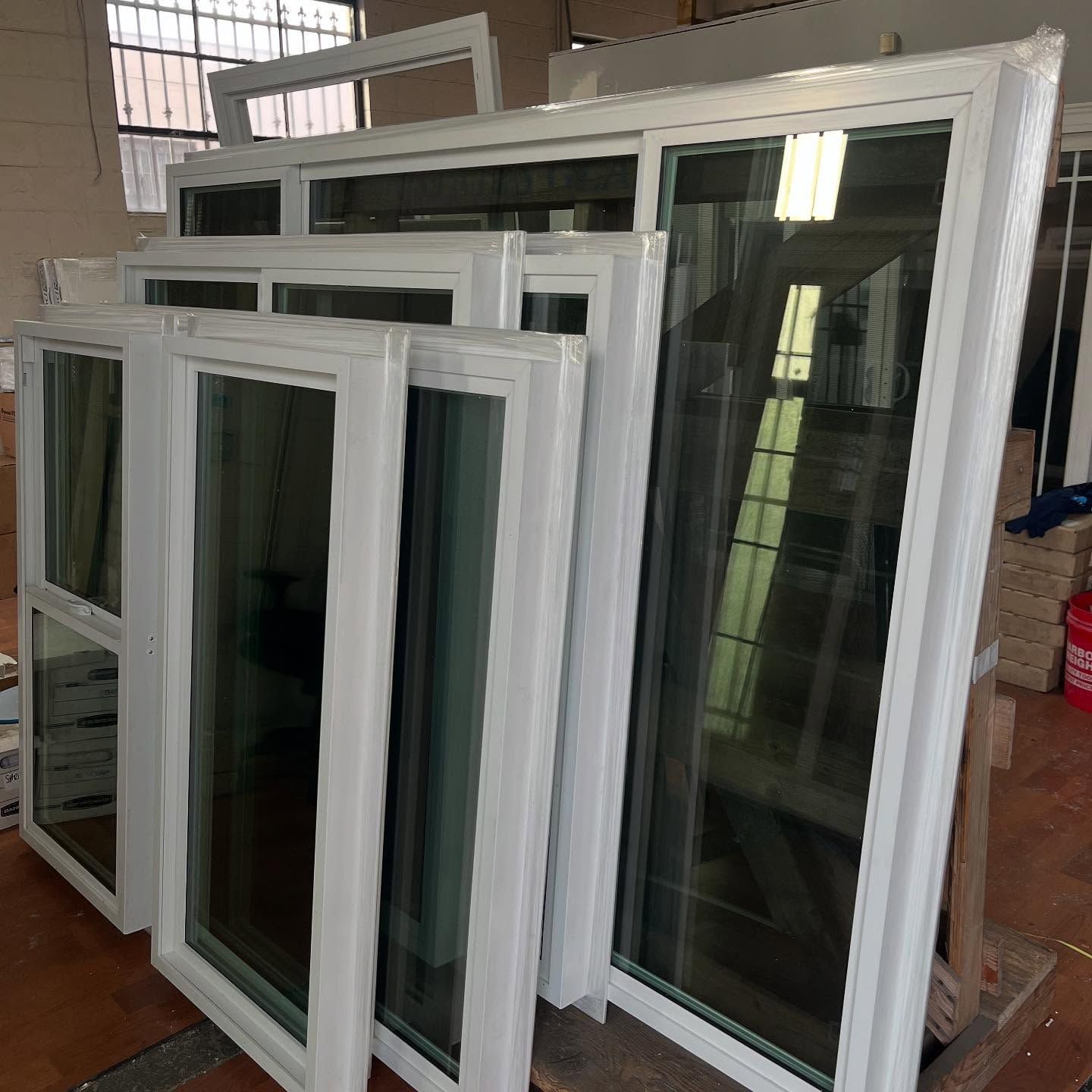 Stacked white-framed windows leaning inside a workshop, with glass panes reflecting light.