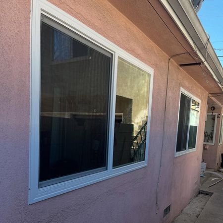 Pink stucco house exterior with two white-framed windows along a side walkway