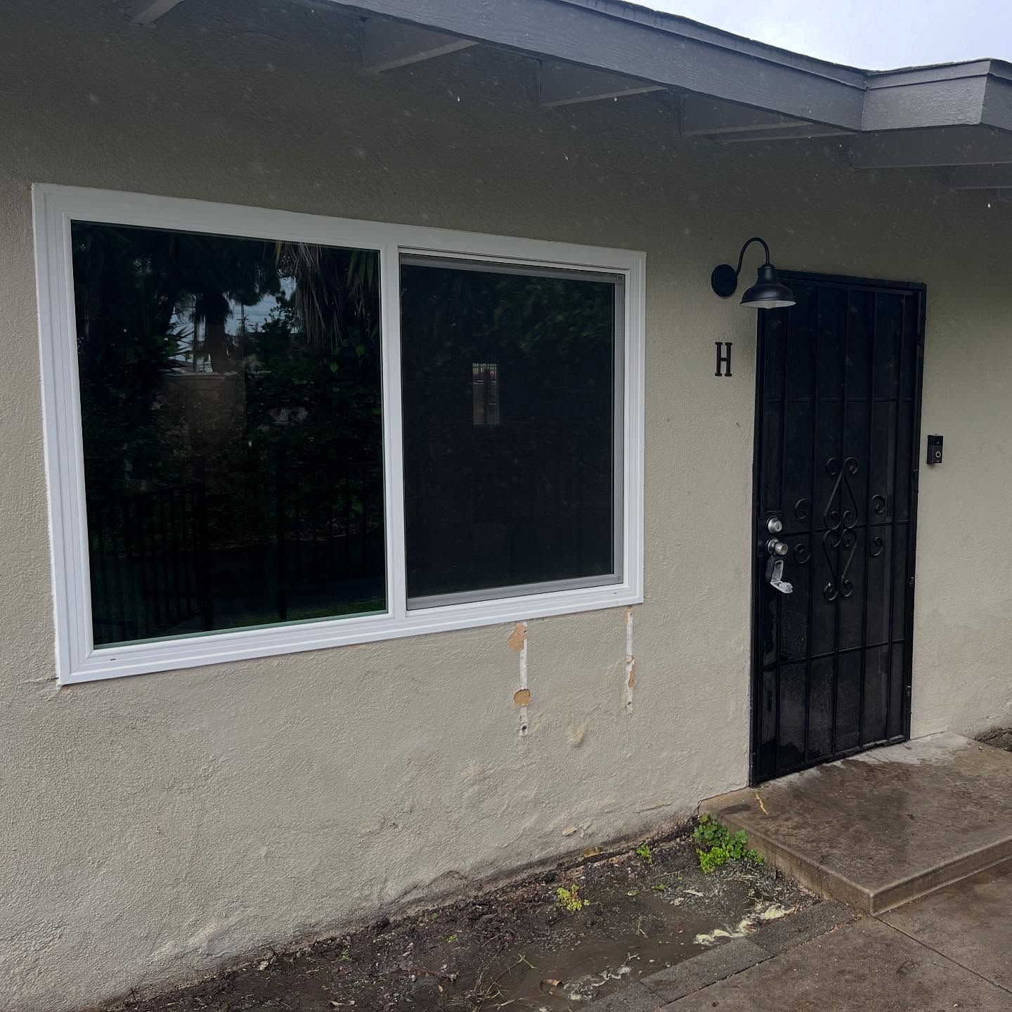 Gray house exterior with large window and black metal security door beside a wet walkway.