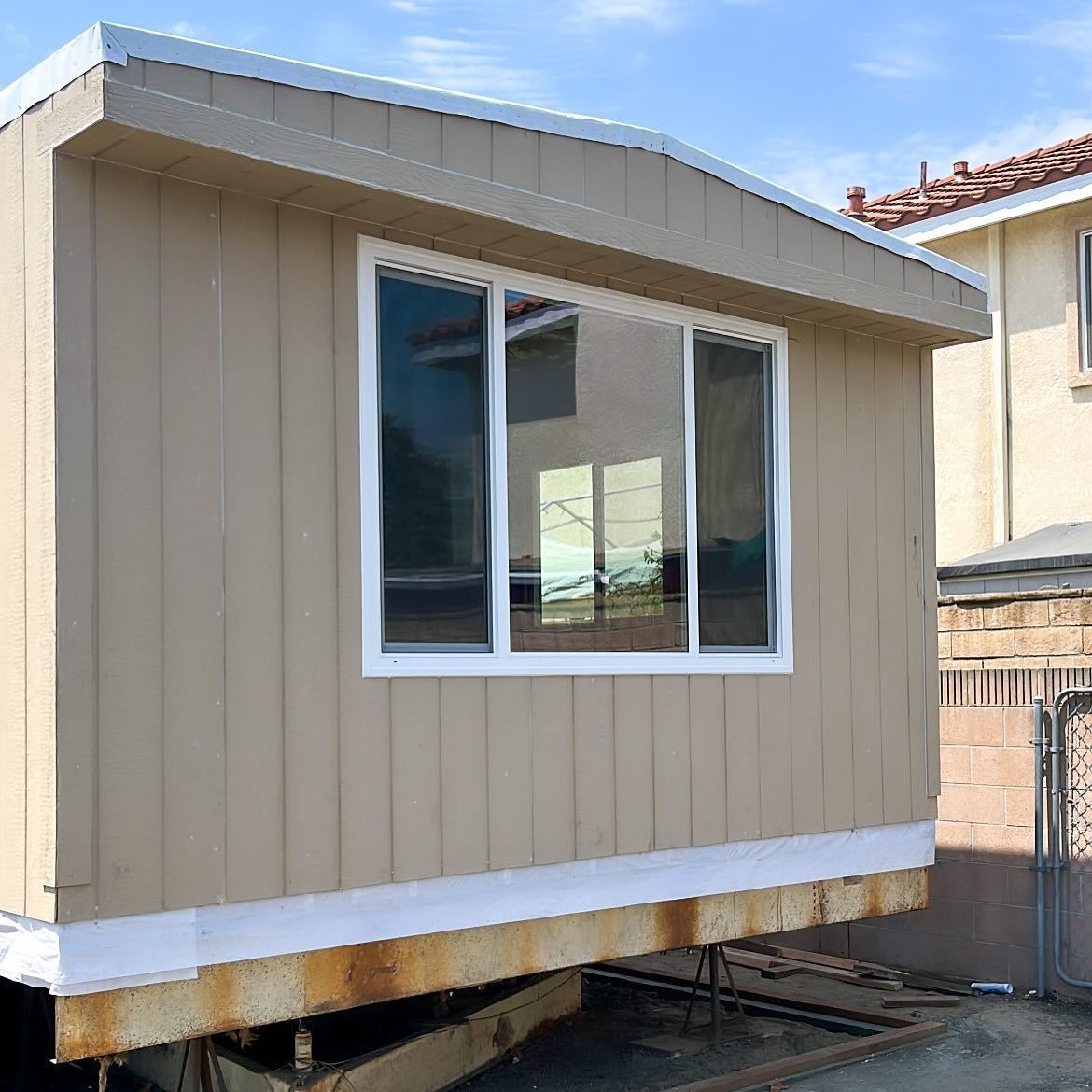 Small beige shed with white trim and a window, elevated on supports in a yard.