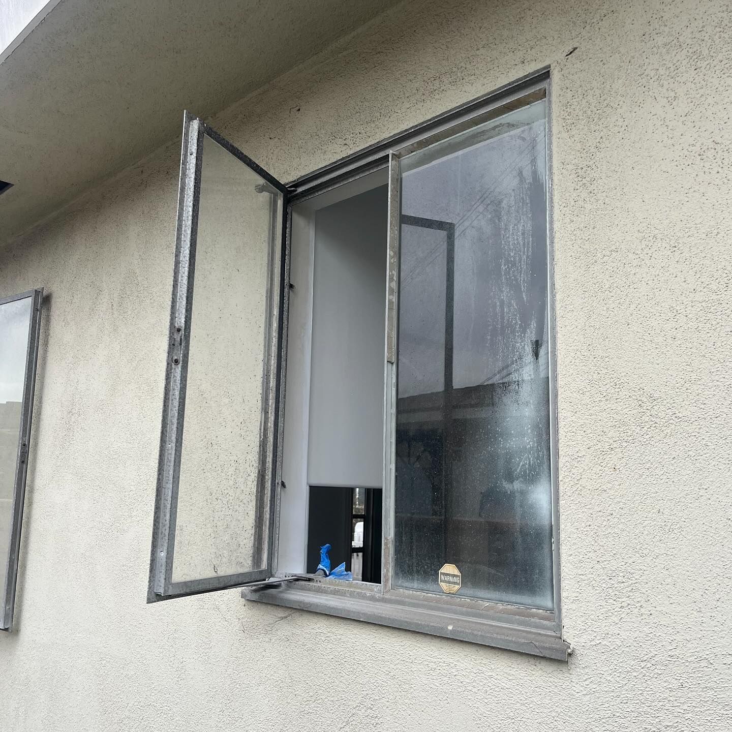 Open window in beige exterior wall, with a small shelf and items on the sill inside