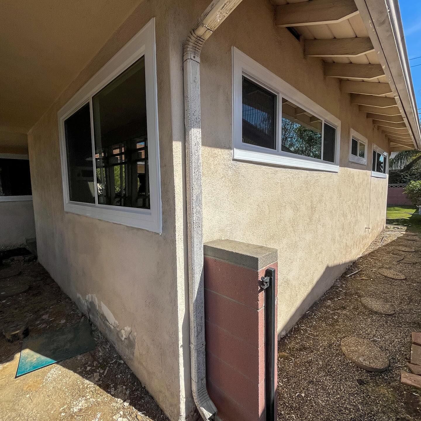 Beige stucco house exterior with white-trimmed windows and a small utility door by the corner.