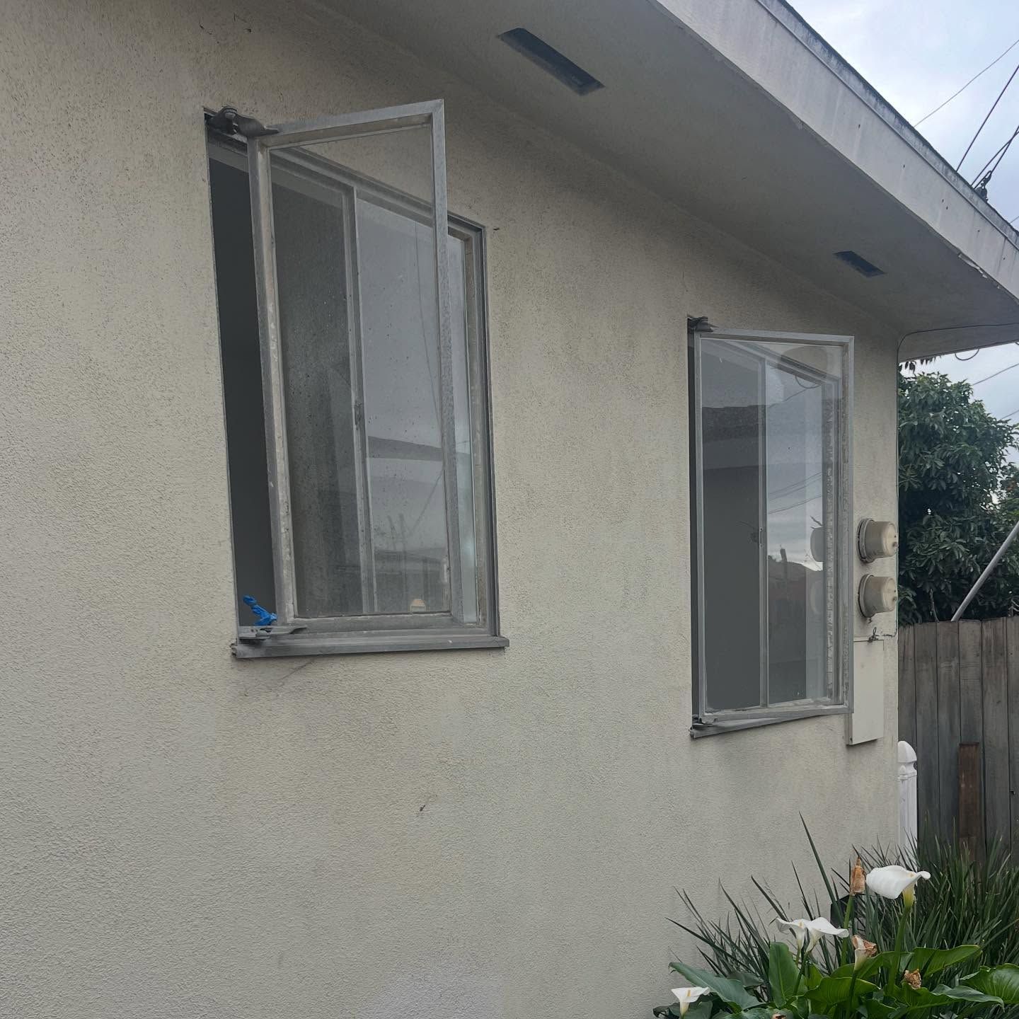 Two open windows on a stucco house wall, with a small garden below.