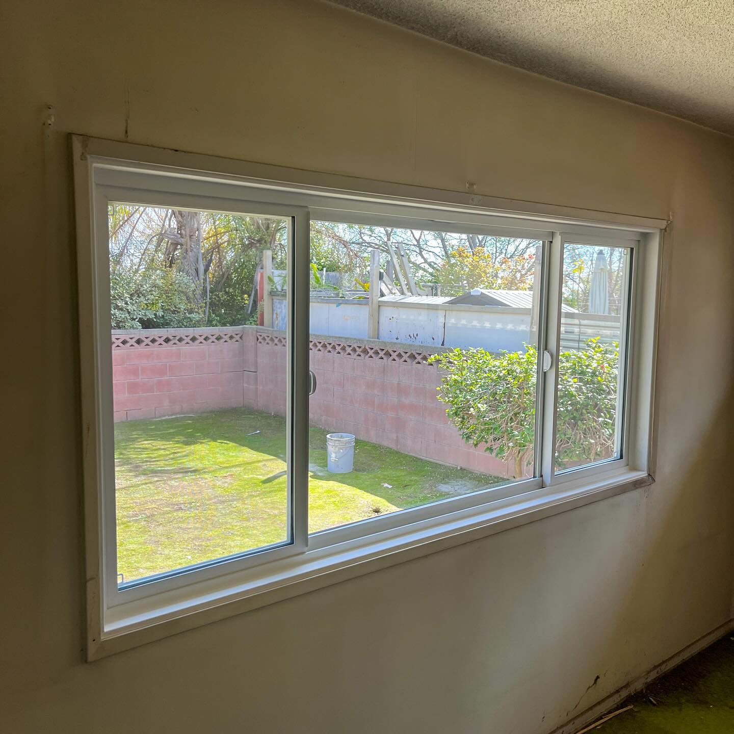 Empty room with a wide window overlooking a pink-walled backyard and green lawn