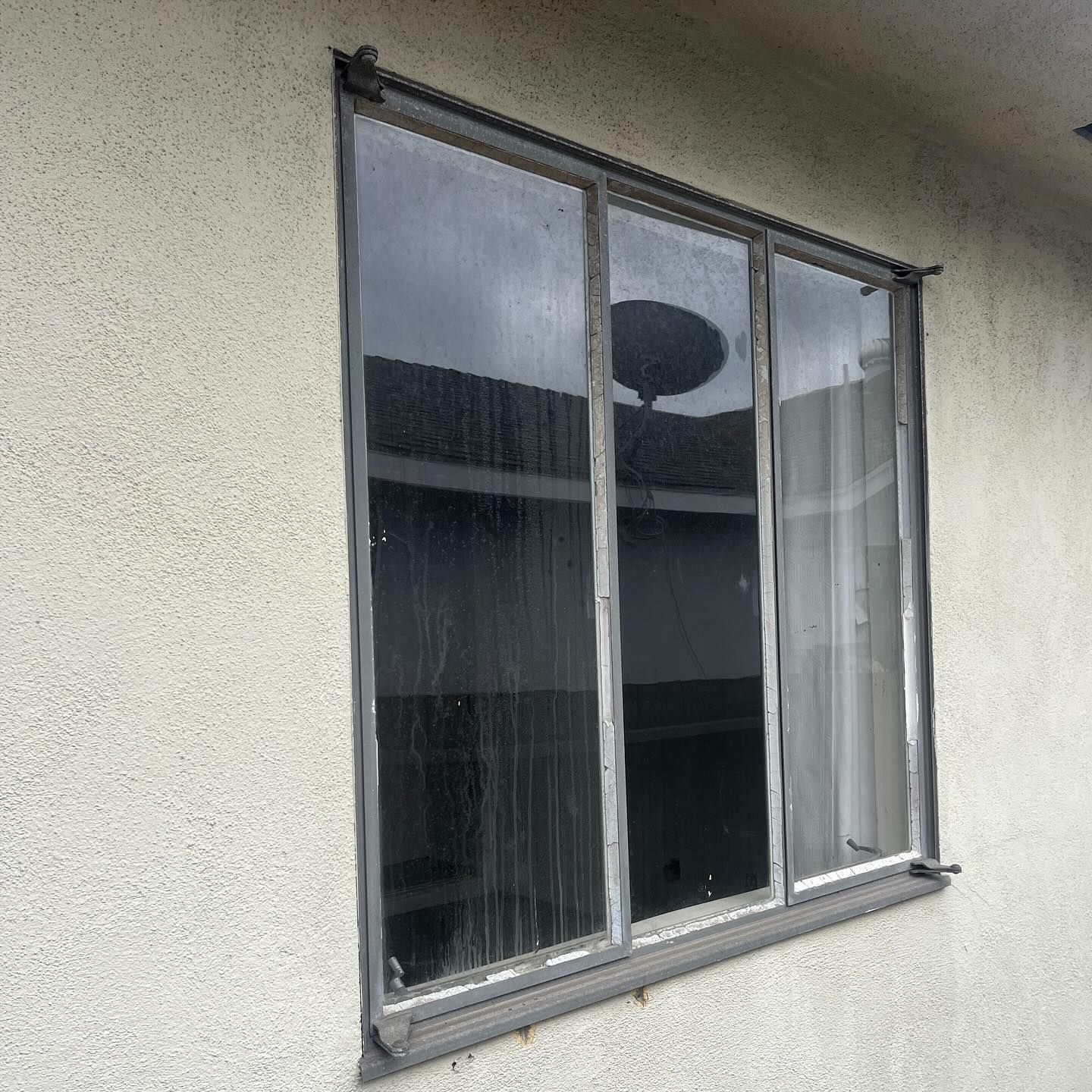 Gray-framed sliding window set in a beige stucco wall, reflecting a dark interior.