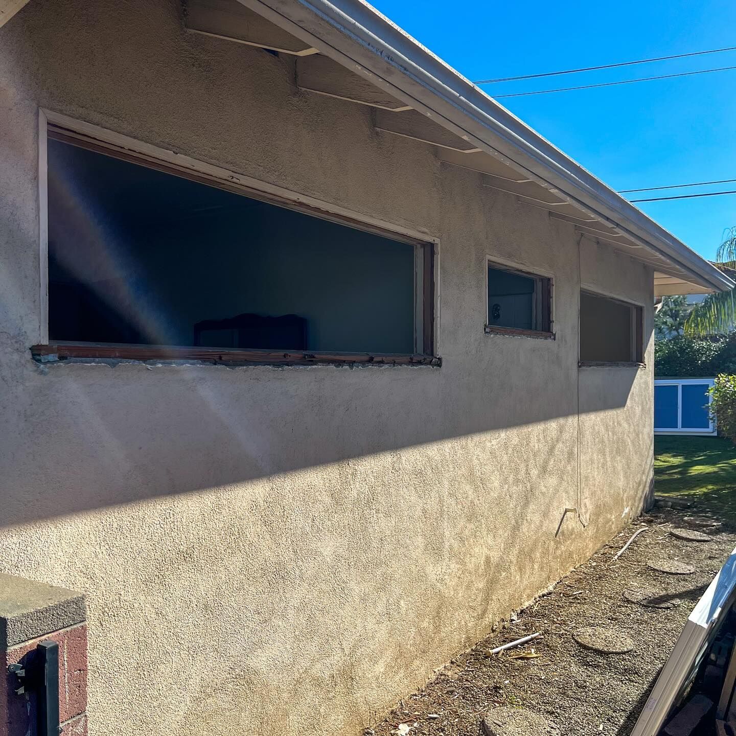 Exterior side of a beige stucco house with windows under a blue sky