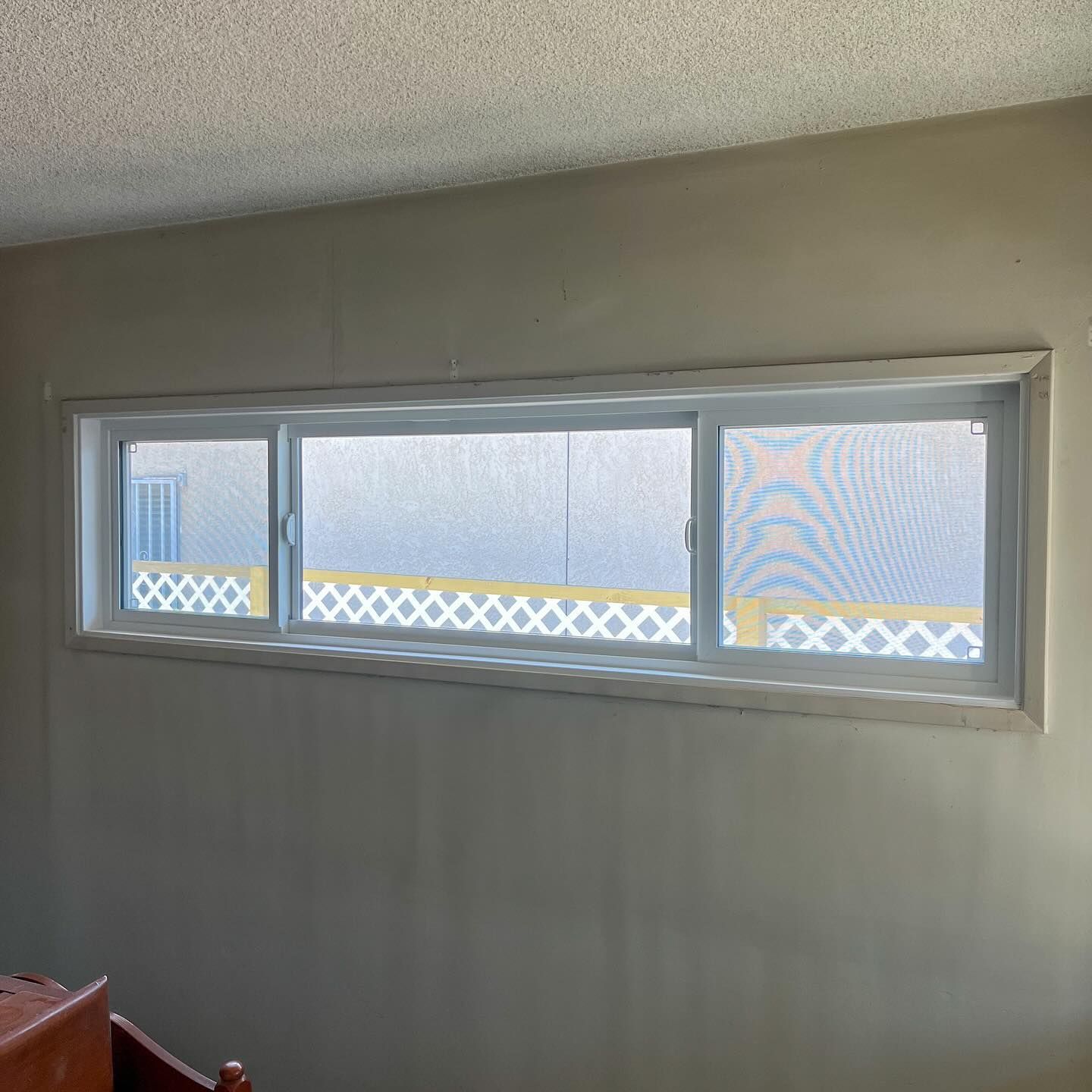 Three-pane window set into a gray wall, with frosted glass and diamond-pattern privacy film outside.