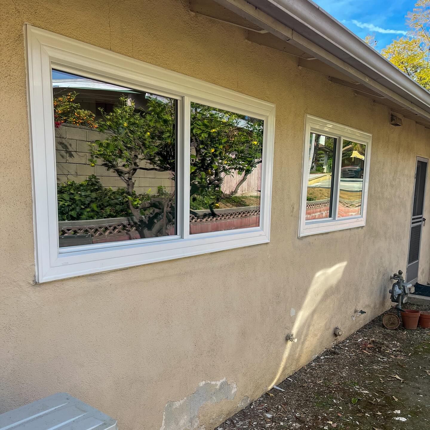 Tan stucco house exterior with two white-framed windows reflecting trees and sky
