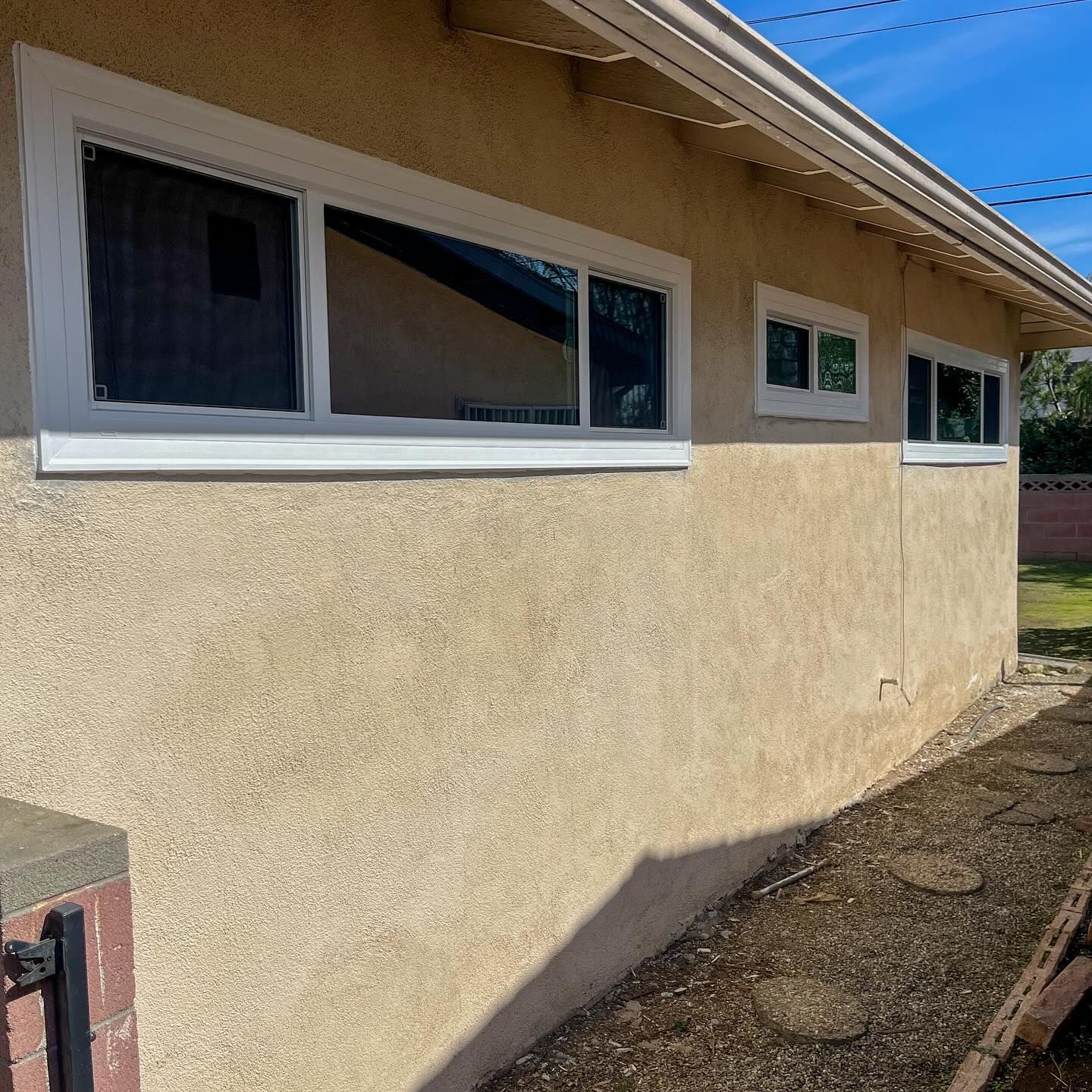 Exterior stucco wall of a house with white-trimmed windows under a clear blue sky