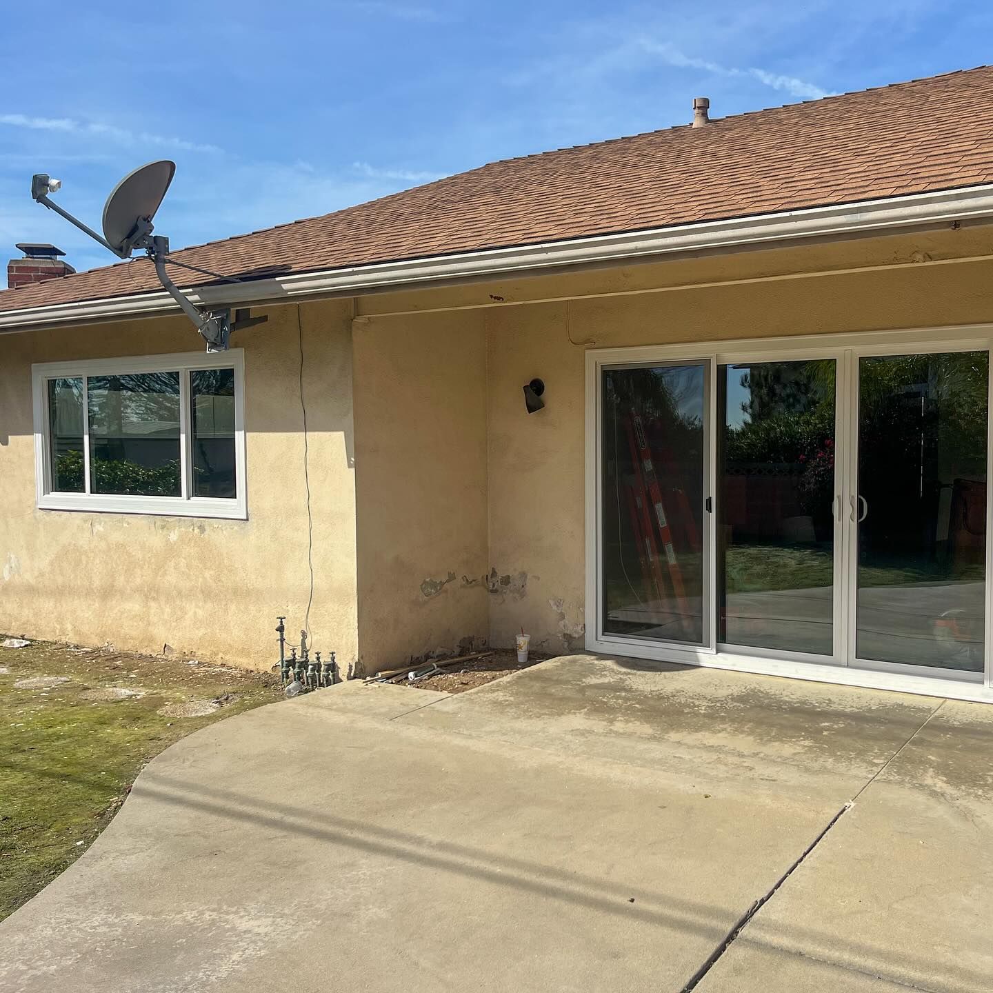Back patio with sliding glass doors, beige stucco wall, and tiled roof under a sunny sky