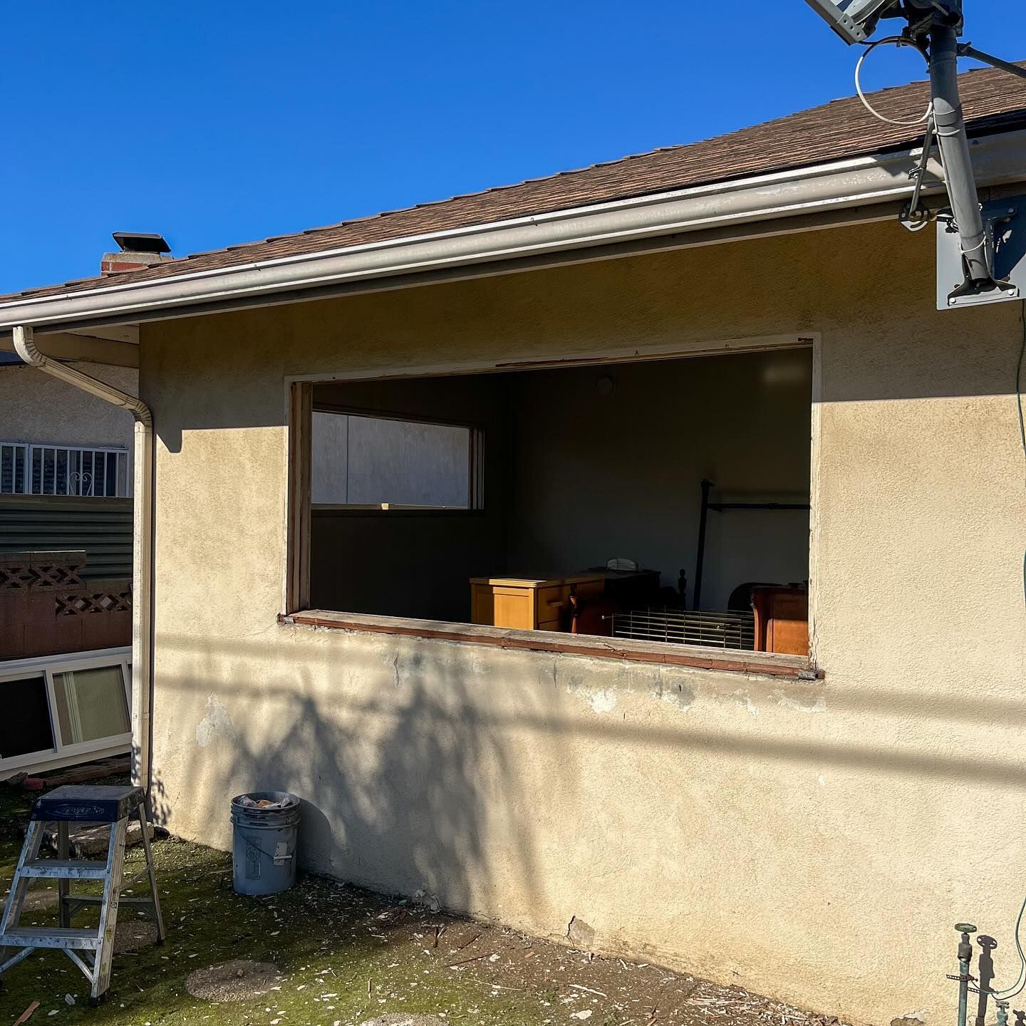 Exterior of a beige house with a covered patio, open window, and a ladder in the yard